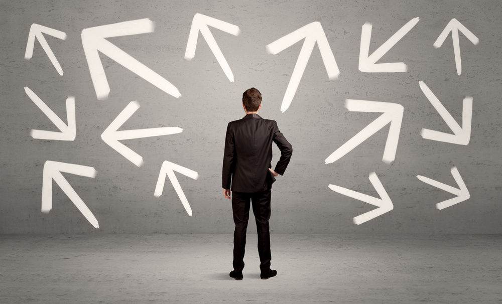 An elegant businessman standing with his back in front of urban wall full of arrows pointing in different directions concept-1