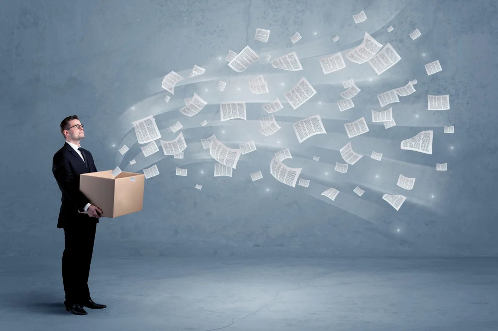 Office documents, contracts, papers flying out of cardboard box being held by a young business worker concept
