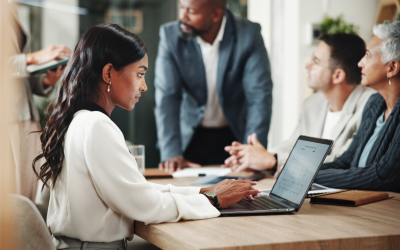 Woman typing on her laptop at a desk with other people.