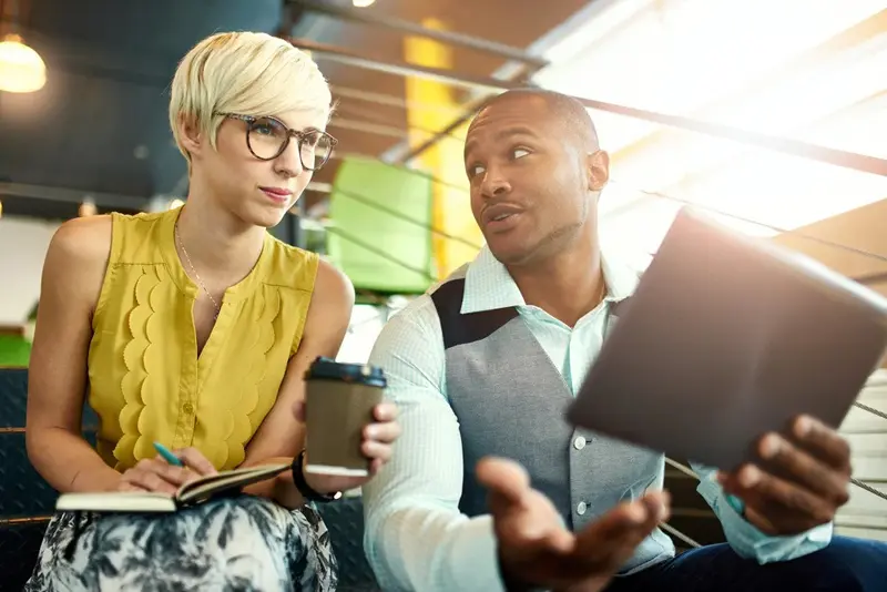 wo creative millenial small business owners working on social media strategy using a digital tablet while sitting in staircase